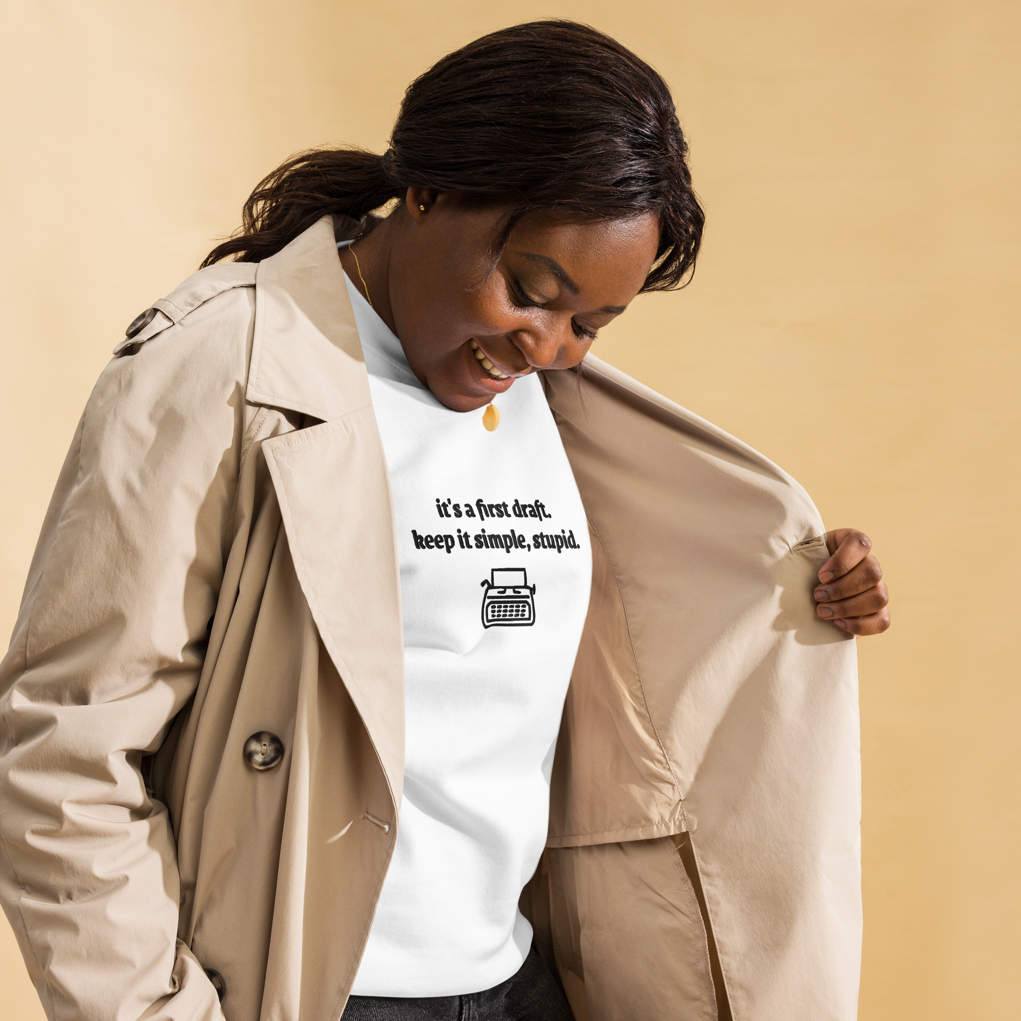 Person wearing a beige trench coat over a white t-shirt with text and a typewriter graphic on a beige background